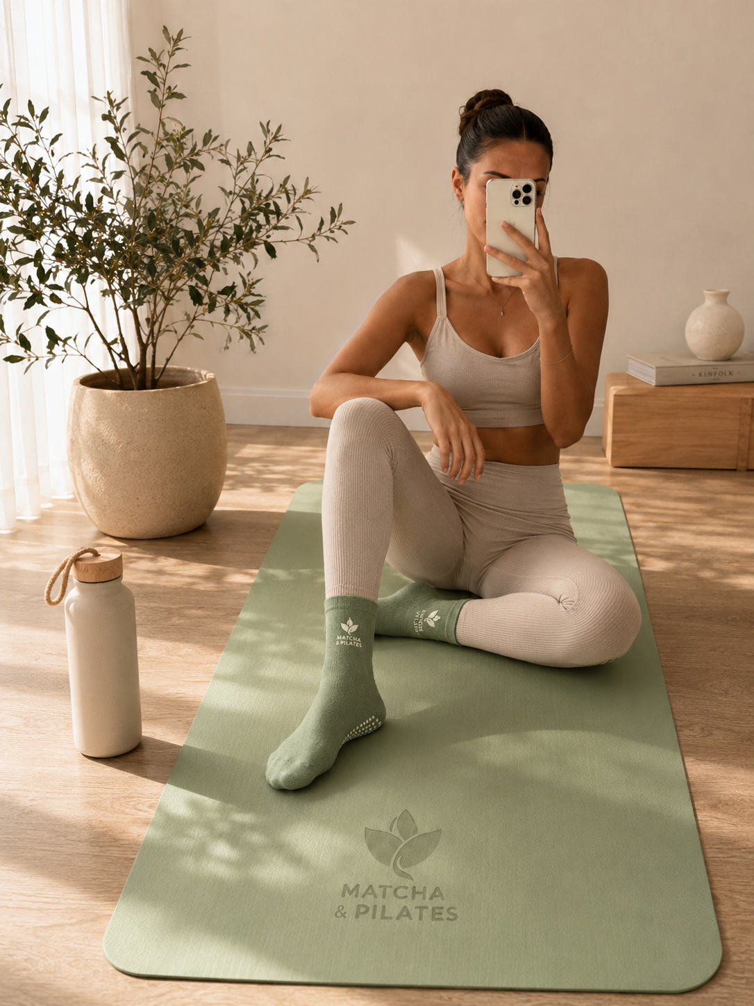 Femme en tenue de yoga assise sur un tapis de pilates vert avec chaussettes de sport.