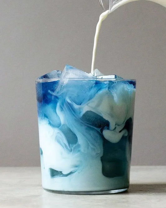 Boisson glacée au lait bleu avec glaçons dans un verre transparent.